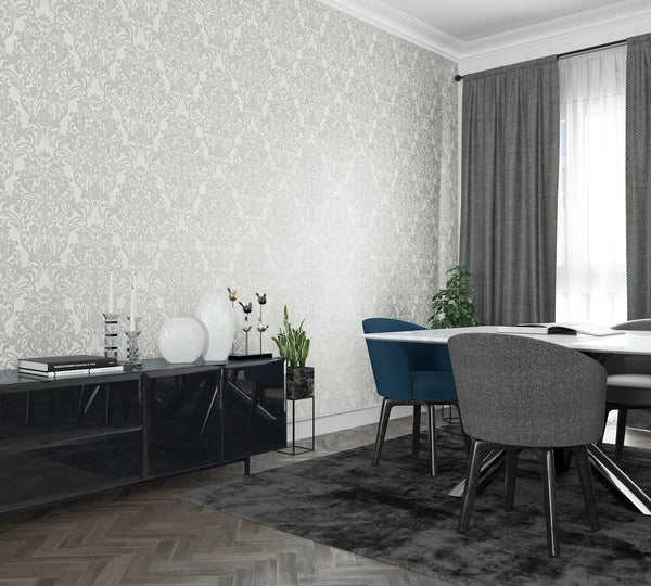 Marburg City Glam 32602 Room scene with a white wall covered in light gray damask wallpaper behind a dining table with blue and gray chairs, a black sideboard with decor, a window with gray curtains, a rug, and indoor plants.