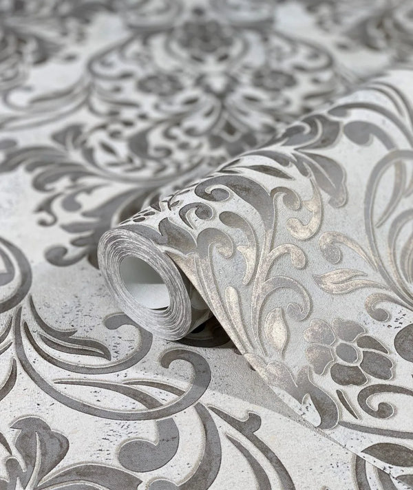 Marburg City Glam 32603 A wallpaper roll on the matching surface, showing a large gray damask scroll and floral pattern with tonal shading.