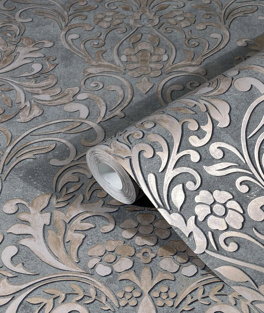 Marburg City Glam 32604 Close-up of a wallpaper roll on a matching surface, showing a large ornate damask floral and scroll pattern in light beige on gray.