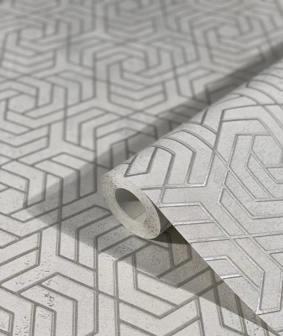 Marburg City Glam 32607 Close-up of a gray wallpaper roll with a raised interlocking geometric pattern resting on the same design.