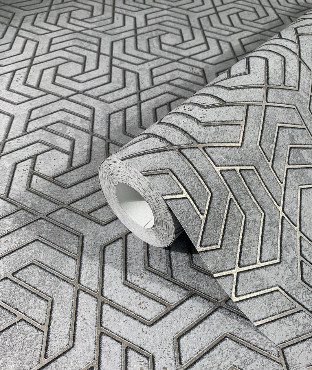 Marburg City Glam 32610 A roll of gray wallpaper on a matching surface, showing a raised interlocking chevron geometric pattern with a mottled background.