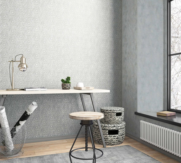 Marburg City Glam 32610 Light gray wallpaper with an interlocking geometric pattern is shown on a feature wall behind a simple desk and stool beside a window.