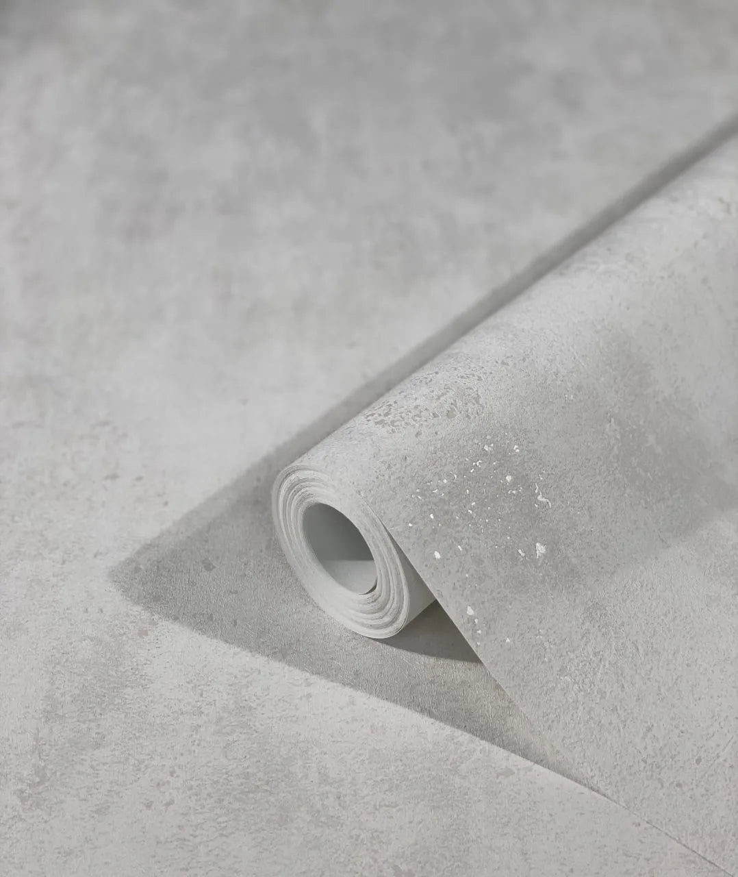 Marburg City Glam 32611 Angled roll of light gray textured wallpaper resting on a matching unrolled sheet, showing a subtle mottled pattern with fine speckling.