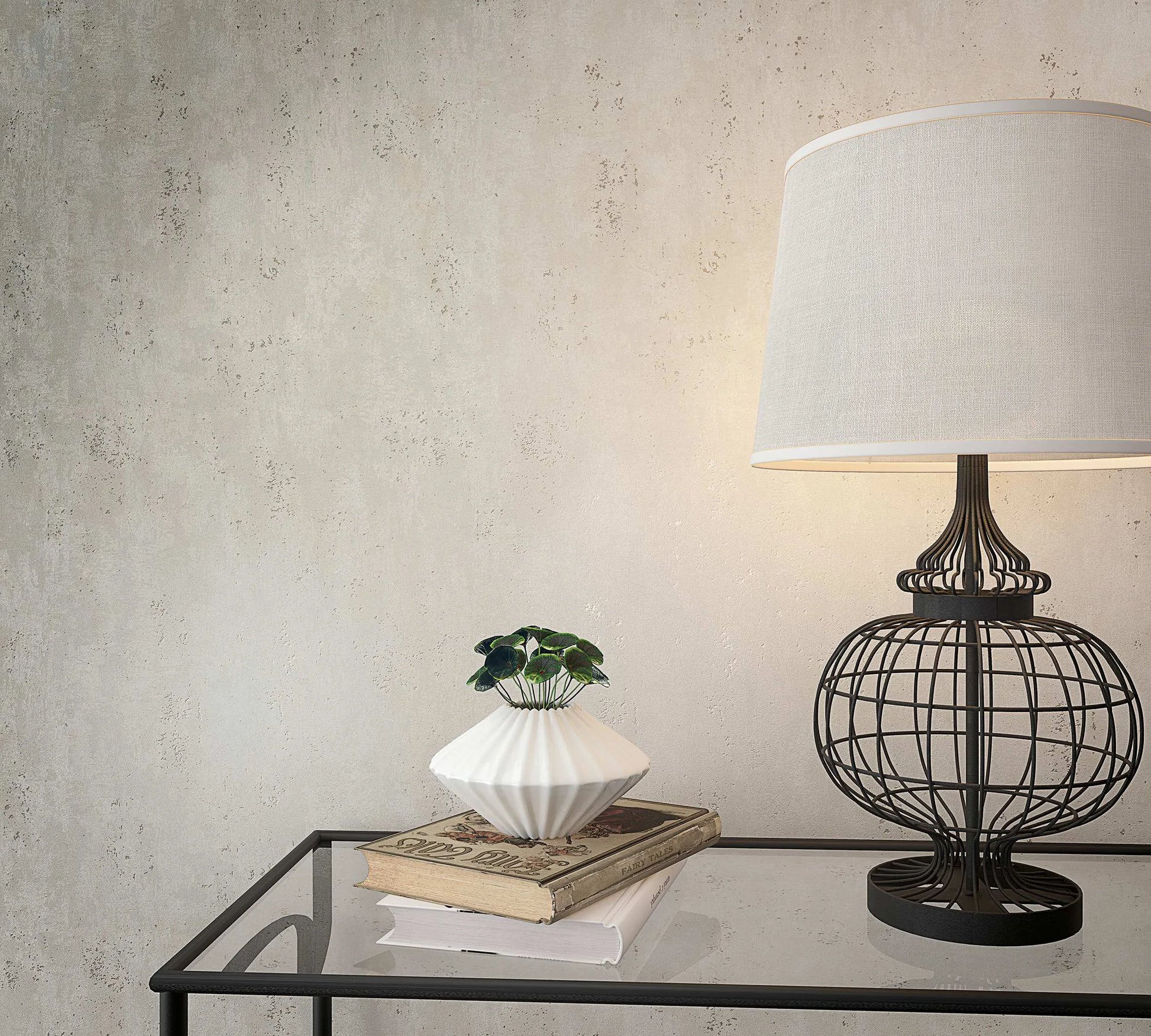 Marburg City Glam 32613 Light gray mottled wallpaper with a subtle plaster look behind a wire-frame table lamp, a small white planter with greenery, and books on a glass-topped table.