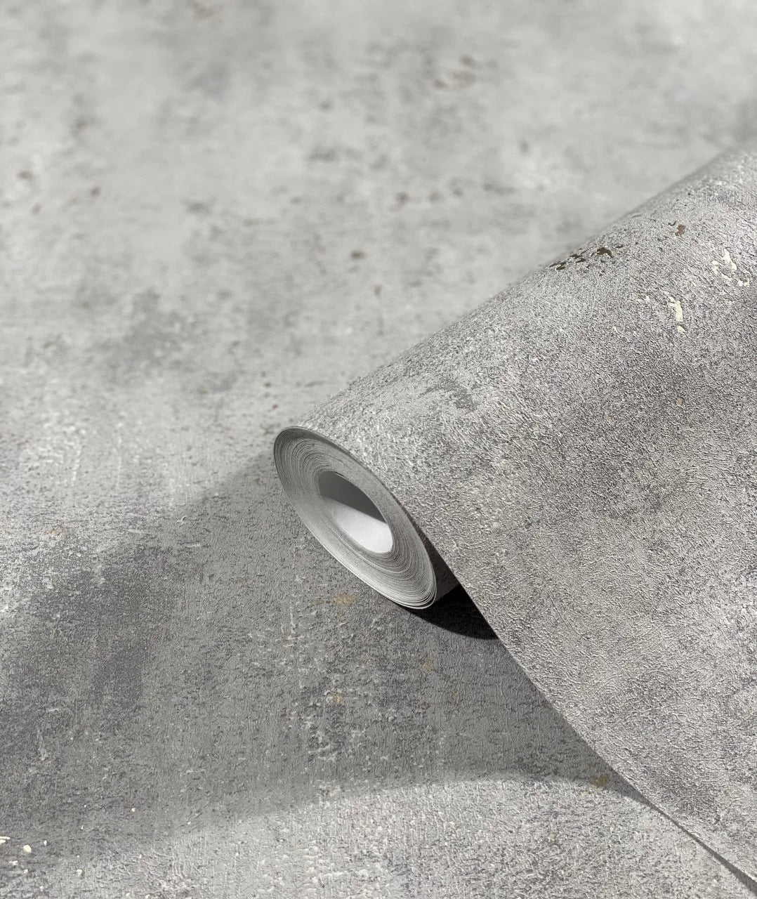 Marburg City Glam 32614 A gray textured wallpaper roll resting on a matching unrolled sheet, showing a concrete-like mottled surface.