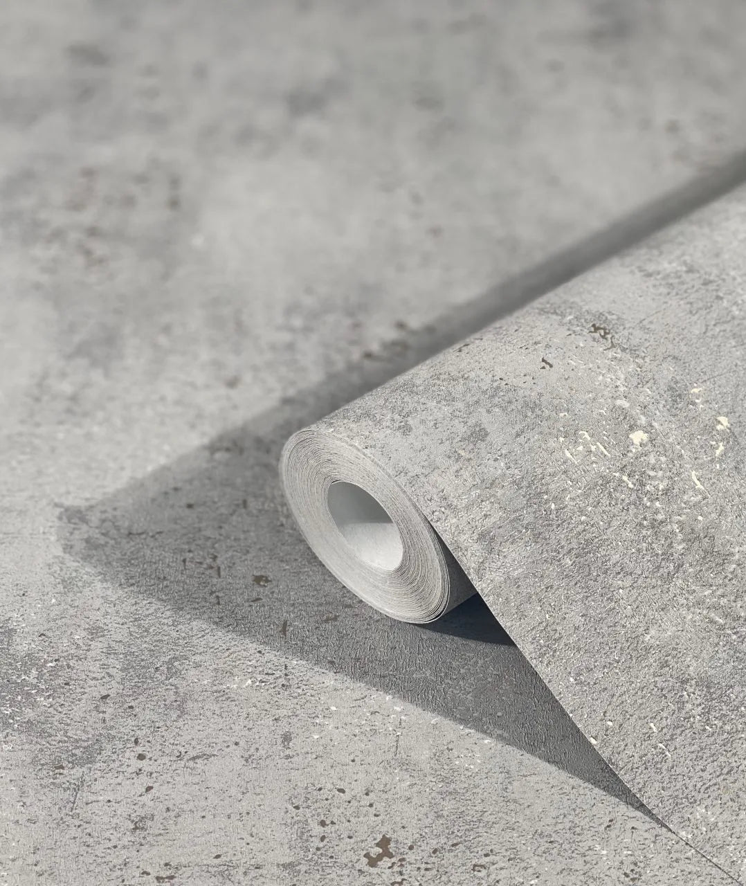 Marburg City Glam 32615 A gray mottled wallpaper roll resting on a matching unrolled sheet, showing a speckled, stone-like texture.