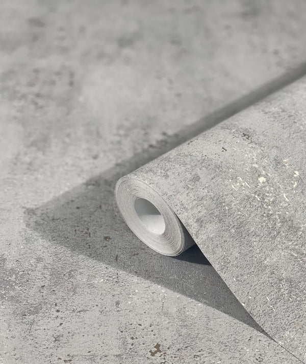 Marburg City Glam 32615 A gray mottled wallpaper roll resting on a matching unrolled sheet, showing a speckled, stone-like texture.