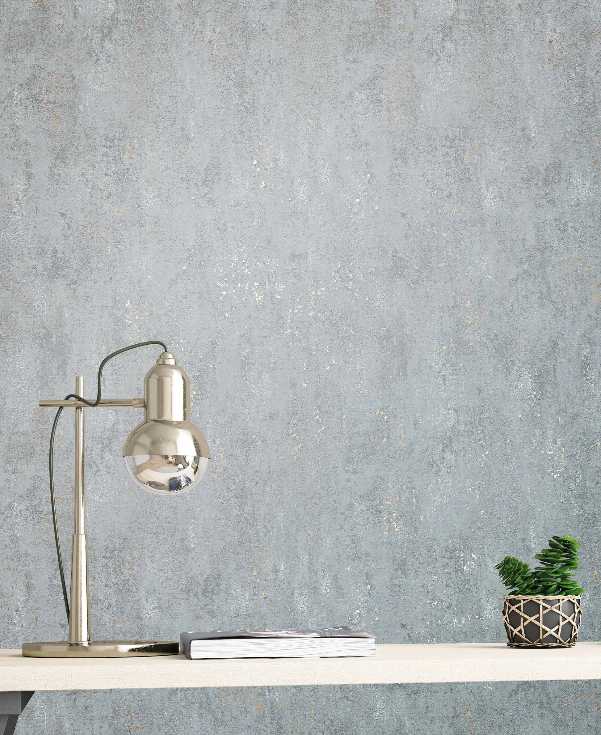 Marburg City Glam 32615 Gray textured wallpaper with faint metallic speckles shown behind a silver desk lamp, a small stack of magazines, and a potted plant on a light shelf.