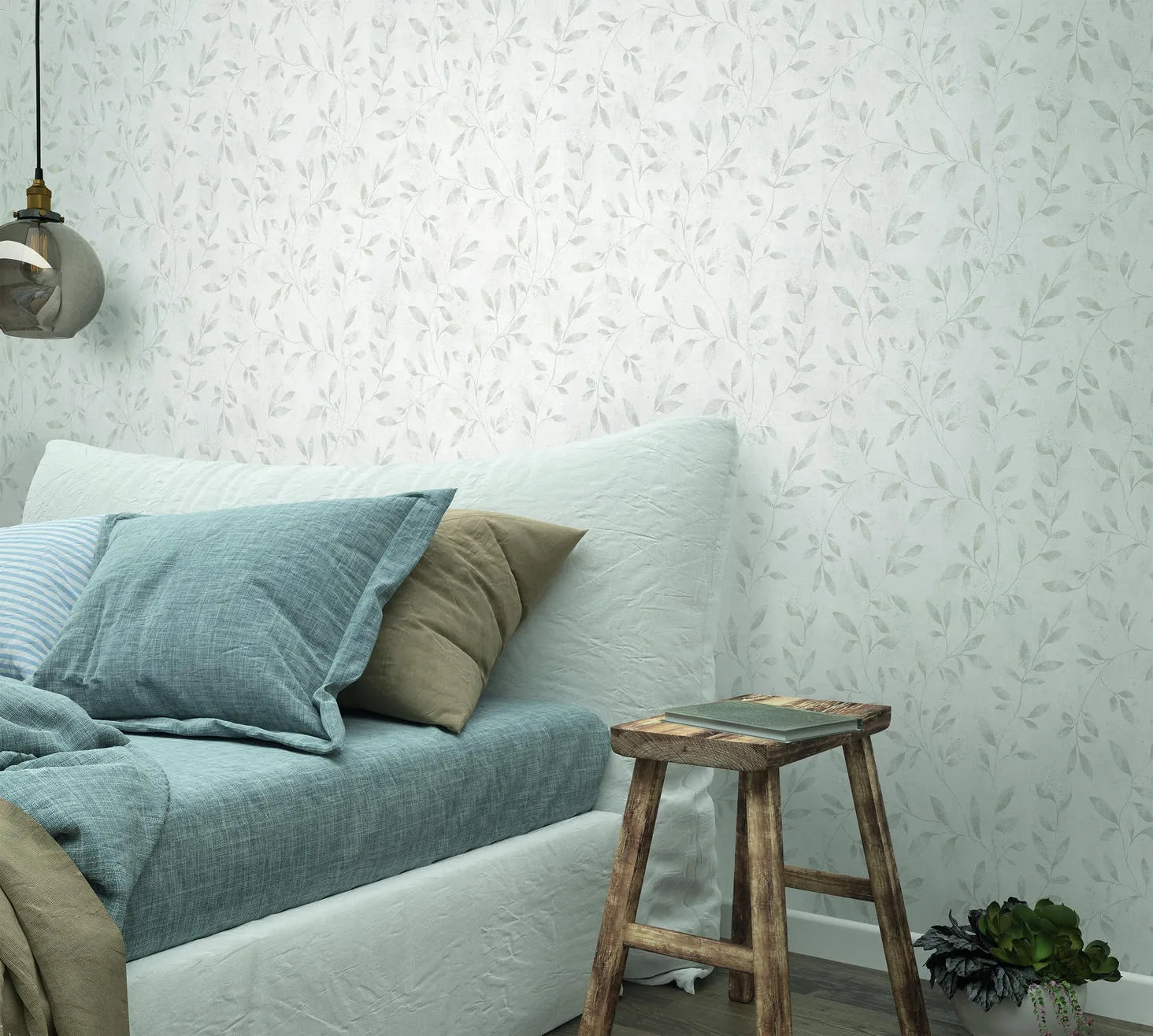 Marburg City Glam 32632 White wallpaper with a delicate leafy vine pattern behind a bed with blue and beige pillows, a rustic wooden stool, a hanging glass pendant light, and a small plant on the floor.