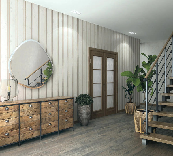 Marburg City Glam 32636 Hallway with light beige vertical striped wallpaper, a wood drawer console with a glass-shade table lamp, an irregular round mirror, potted plants, double doors, and an open staircase.