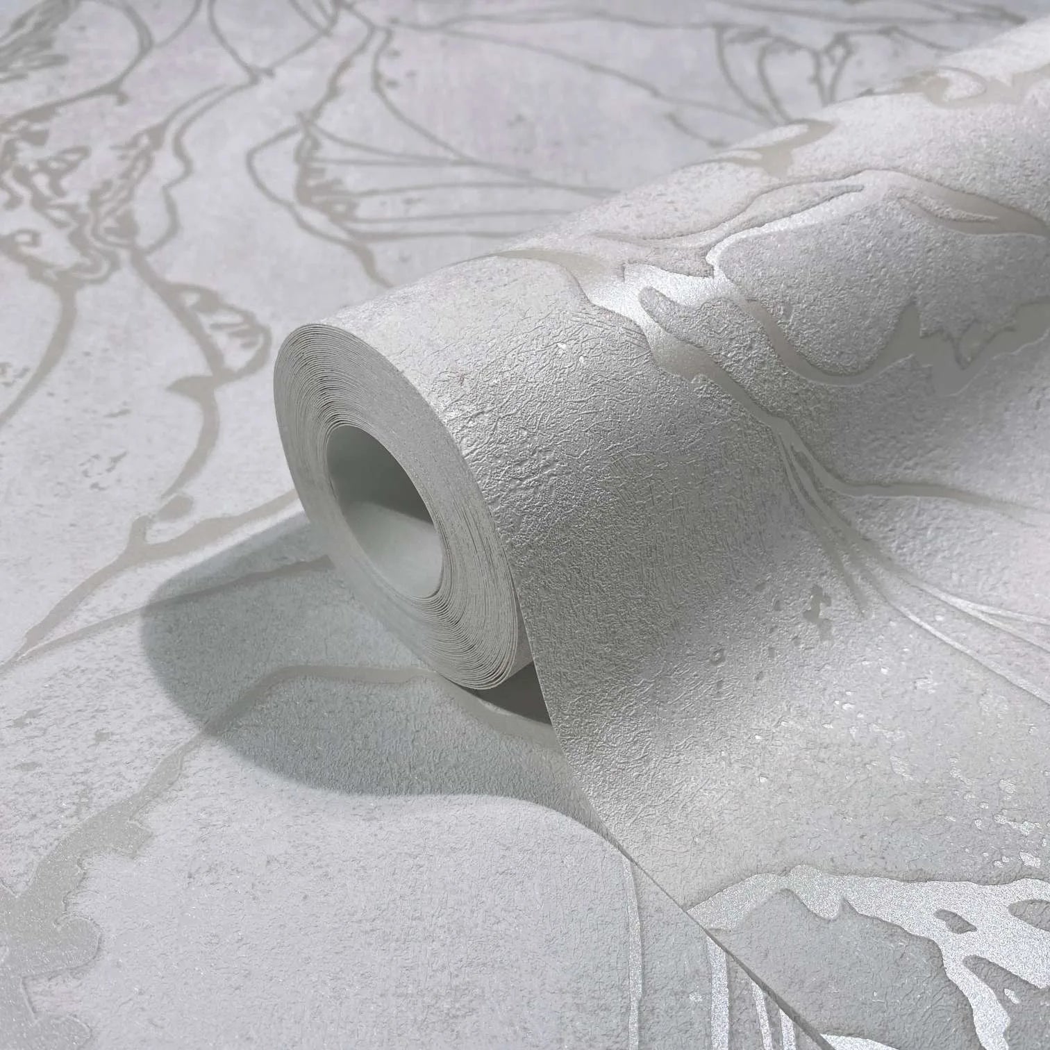 Marburg City Glow 34251 Close-up of a white textured wallpaper roll with metallic abstract line pattern, partially unrolled on the matching surface.