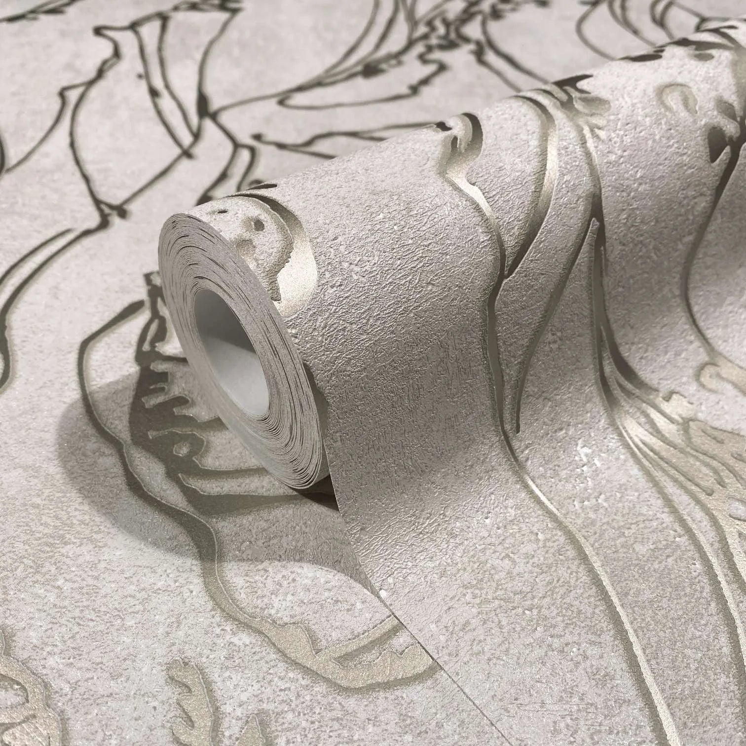 Marburg City Glow 34252 Close-up of a wallpaper roll resting on matching unrolled wallpaper, showing a light neutral textured surface with large flowing embossed outlines.