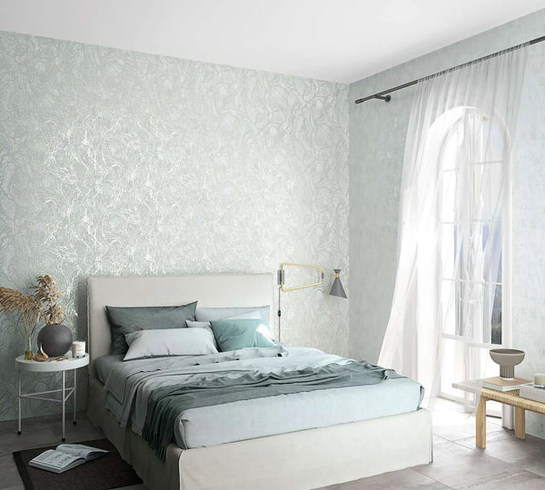 Marburg City Glow 34253 Bedroom scene with a light gray wallpaper featuring an organic swirling pattern on the wall behind an upholstered bed, next to sheer curtains over an arched window.