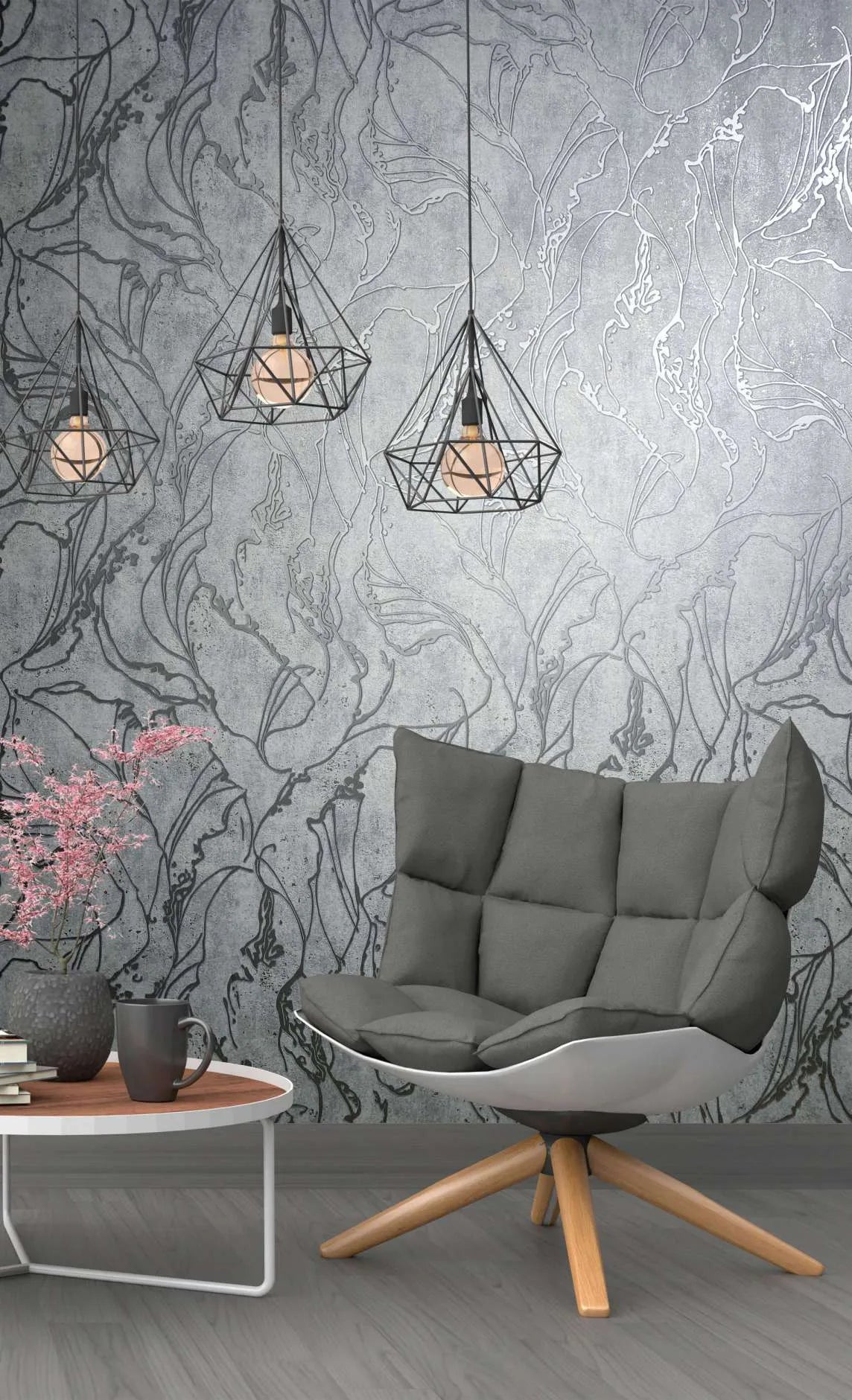 Marburg City Glow 34254 Gray wallpaper with large abstract botanical outlines on a mottled background, shown with geometric pendant lights, a cushioned lounge chair, and a small side table with books, a mug, and a vase of pink flowers.