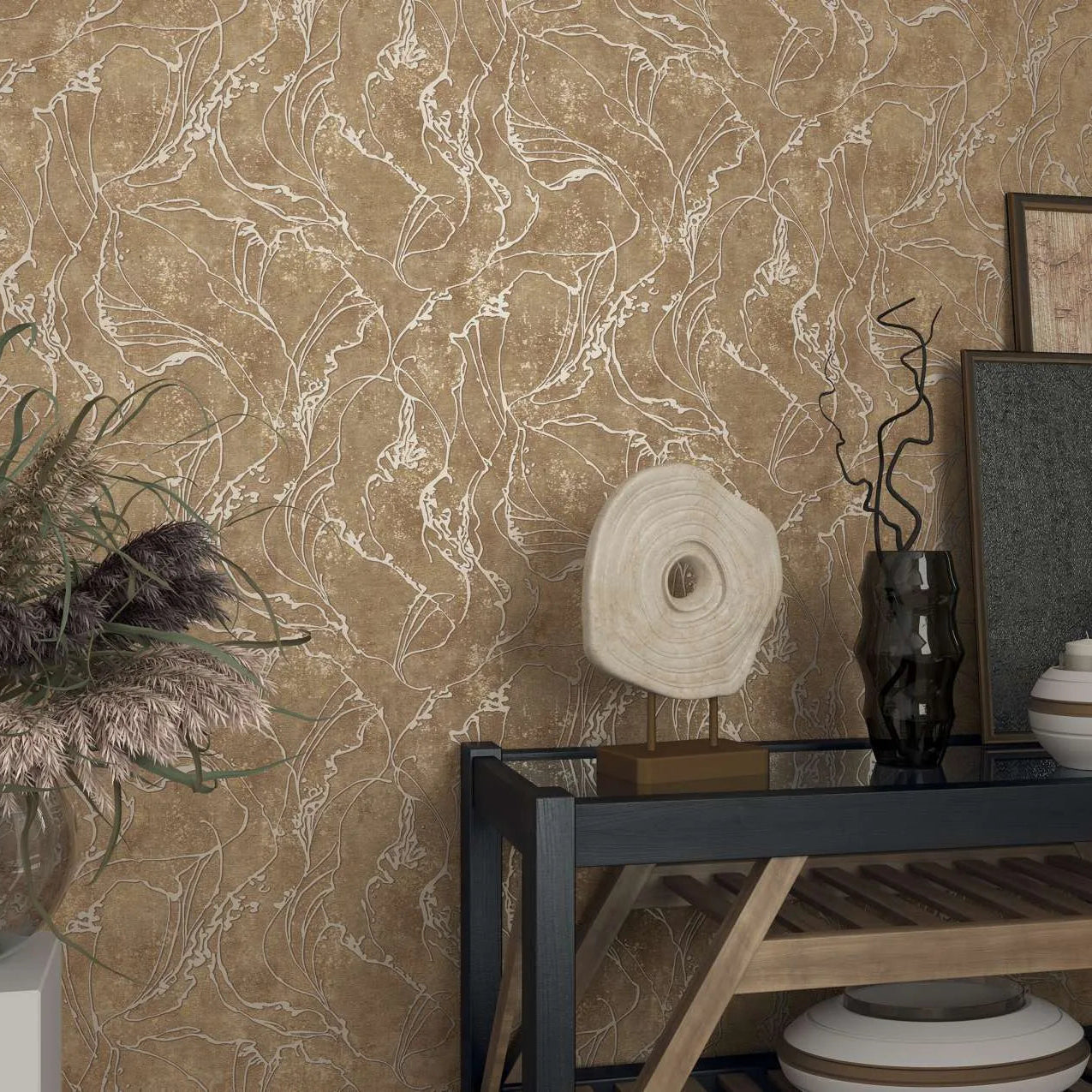 Marburg City Glow 34255 Textured brown wallpaper with flowing abstract leaf-like outlines behind a console vignette with a sculptural disc, dark glass vase, ceramic bowls, framed artwork, and a glass vase of dried grasses.