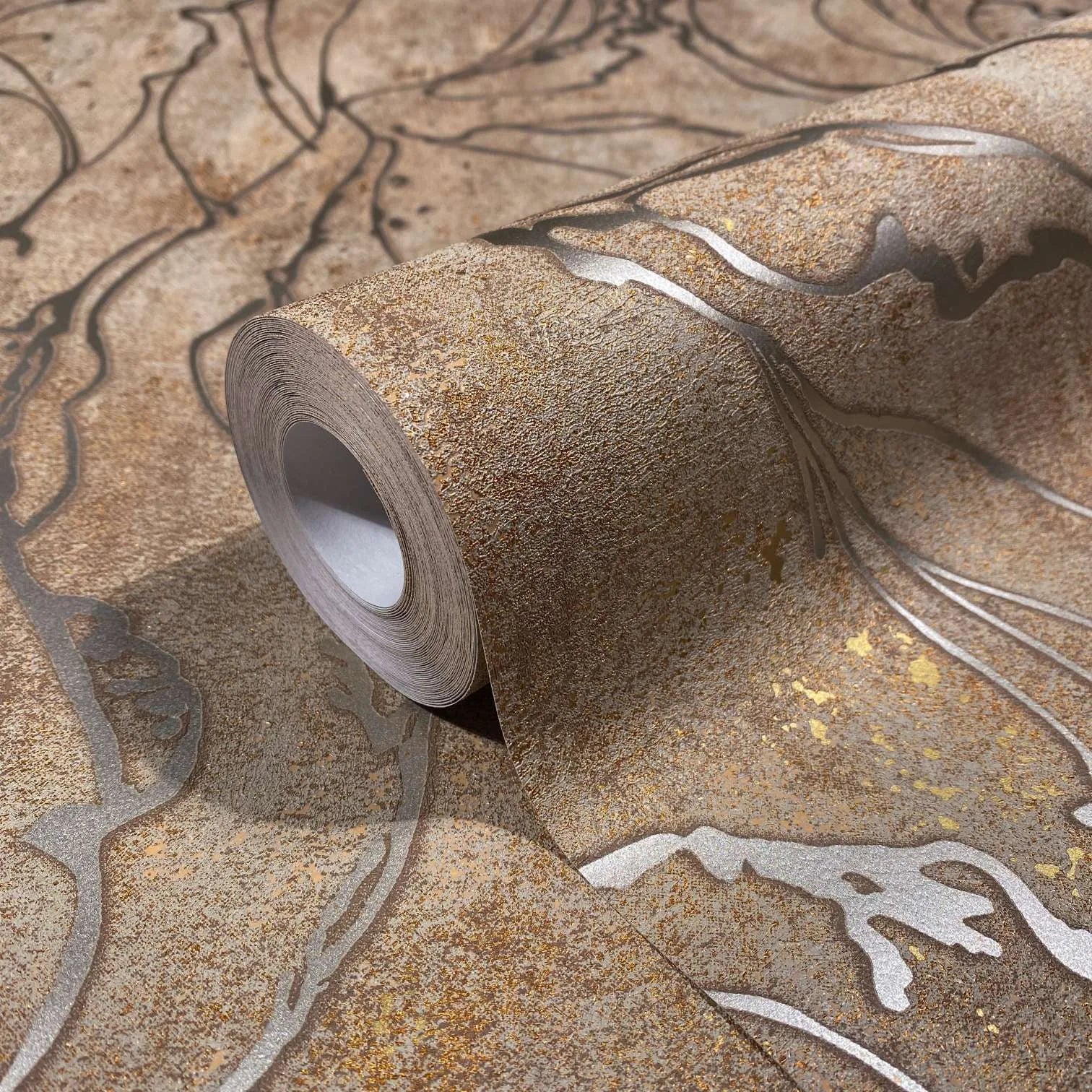 Marburg City Glow 34255 Close-up of a wallpaper roll resting on matching paper, showing a mottled brown ground with flowing metallic lines and small gold speckles.