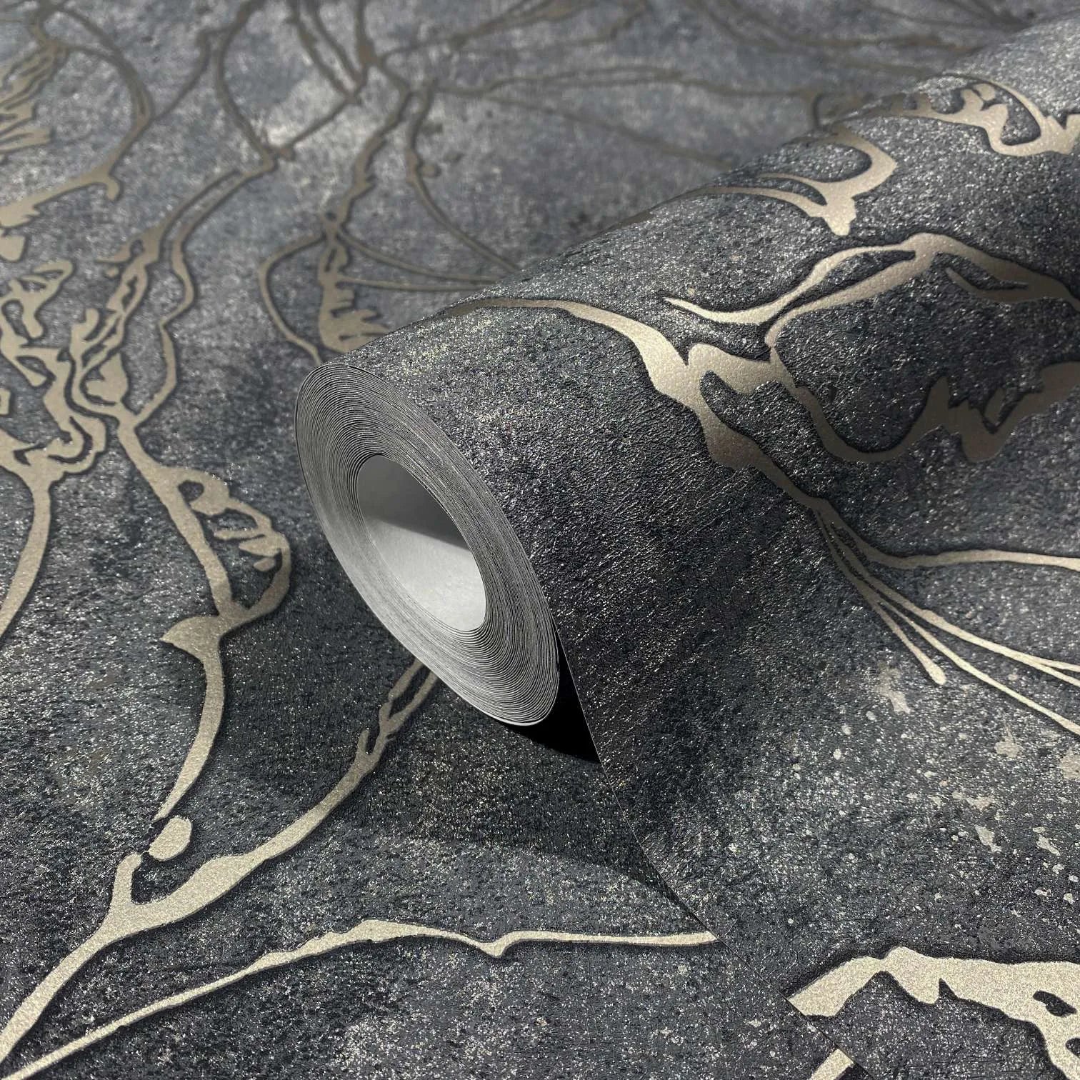 Marburg City Glow 34257 Close-up of a wallpaper roll on the same pattern, showing a dark charcoal background with metallic gold abstract flowing lines and a speckled texture.