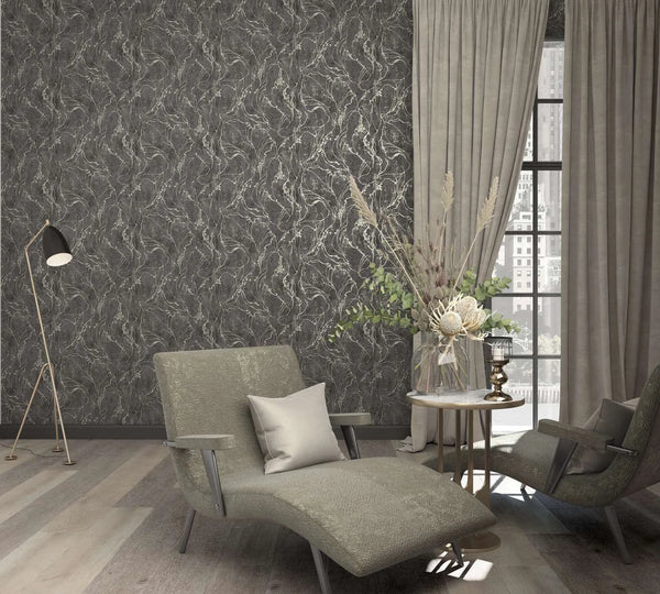 Marburg City Glow 34257 Dark charcoal wallpaper with gold‑toned swirling lines shown in a living room with a chaise and armchair, a side table holding a floral arrangement, a floor lamp, and tall curtains by a window.