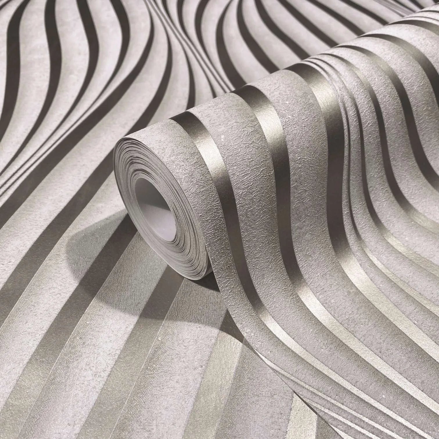Marburg City Glow 34259 Close-up of a wallpaper roll showing a textured ground with flowing metallic wavy stripes, resting on the same pattern.