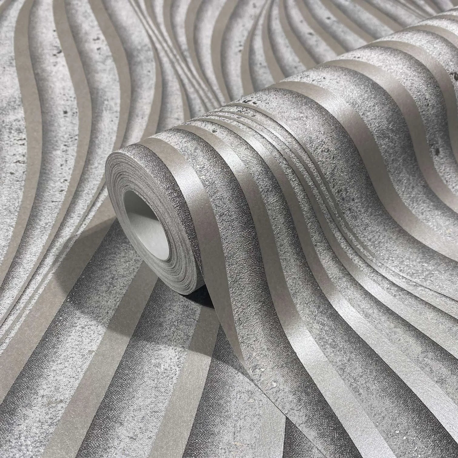 Marburg City Glow 34261 Close-up of a wallpaper roll resting on matching paper, showing a gray wavy striped design with alternating smooth and textured bands.
