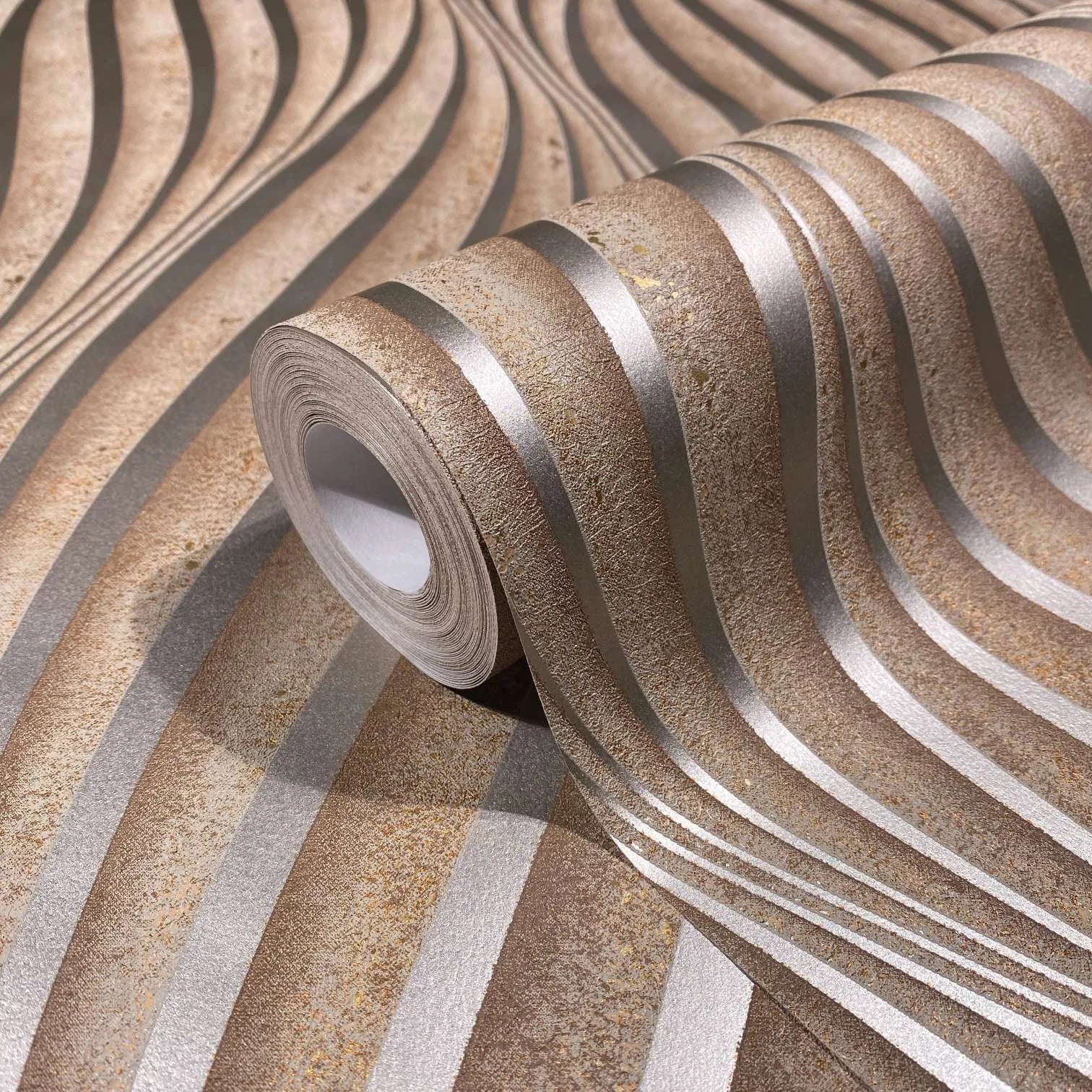 Marburg City Glow 34262 Close-up of a wallpaper roll on matching surface showing undulating brown and light grey stripes with a textured, mottled look.