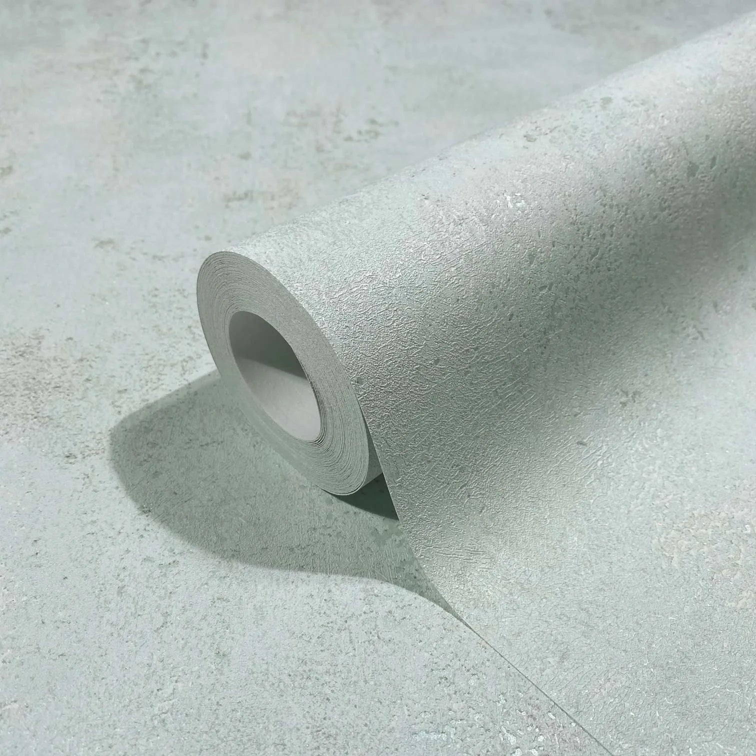 Marburg City Glow 34266 Close-up of a light gray textured wallpaper roll partially unrolled on a matching surface, showing the tonal mottled pattern.
