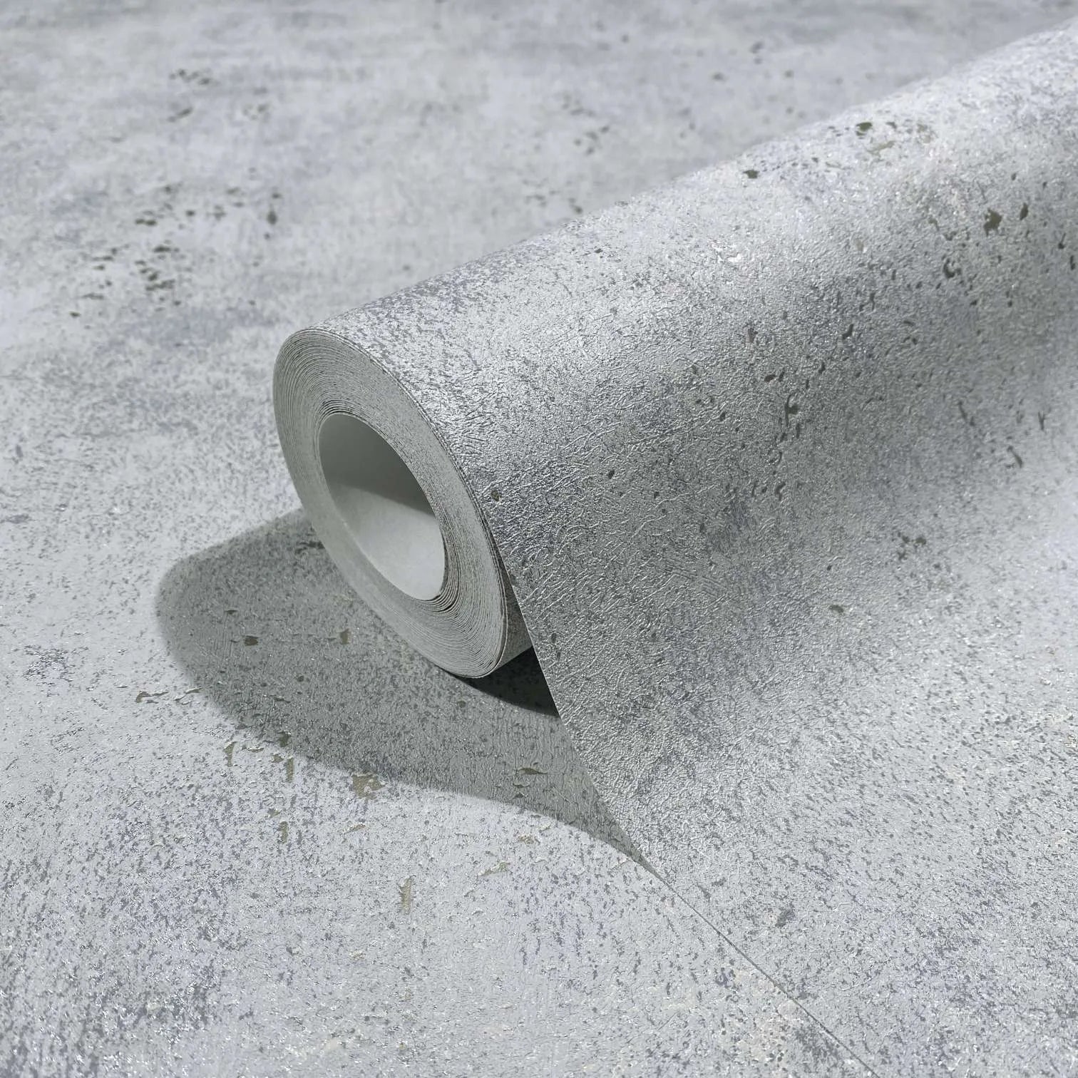 Marburg City Glow 34267 Close-up of a gray textured wallpaper roll resting on the same pattern, showing a mottled concrete-like design with fine speckling.