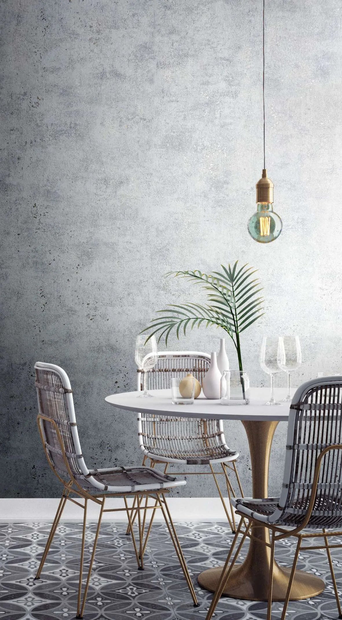 Marburg City Glow 34267 Gray concrete-look textured wallpaper behind a small dining area with a round table, woven chairs, a pendant bulb, glassware, a few vases, a green frond, and a patterned tile floor.