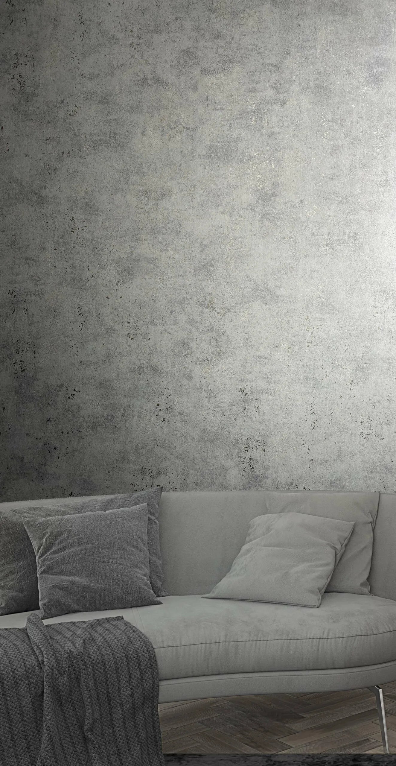 Marburg City Glow 34267 Gray concrete-effect wallpaper behind a gray sofa with pillows and a knit throw on a herringbone wood floor.