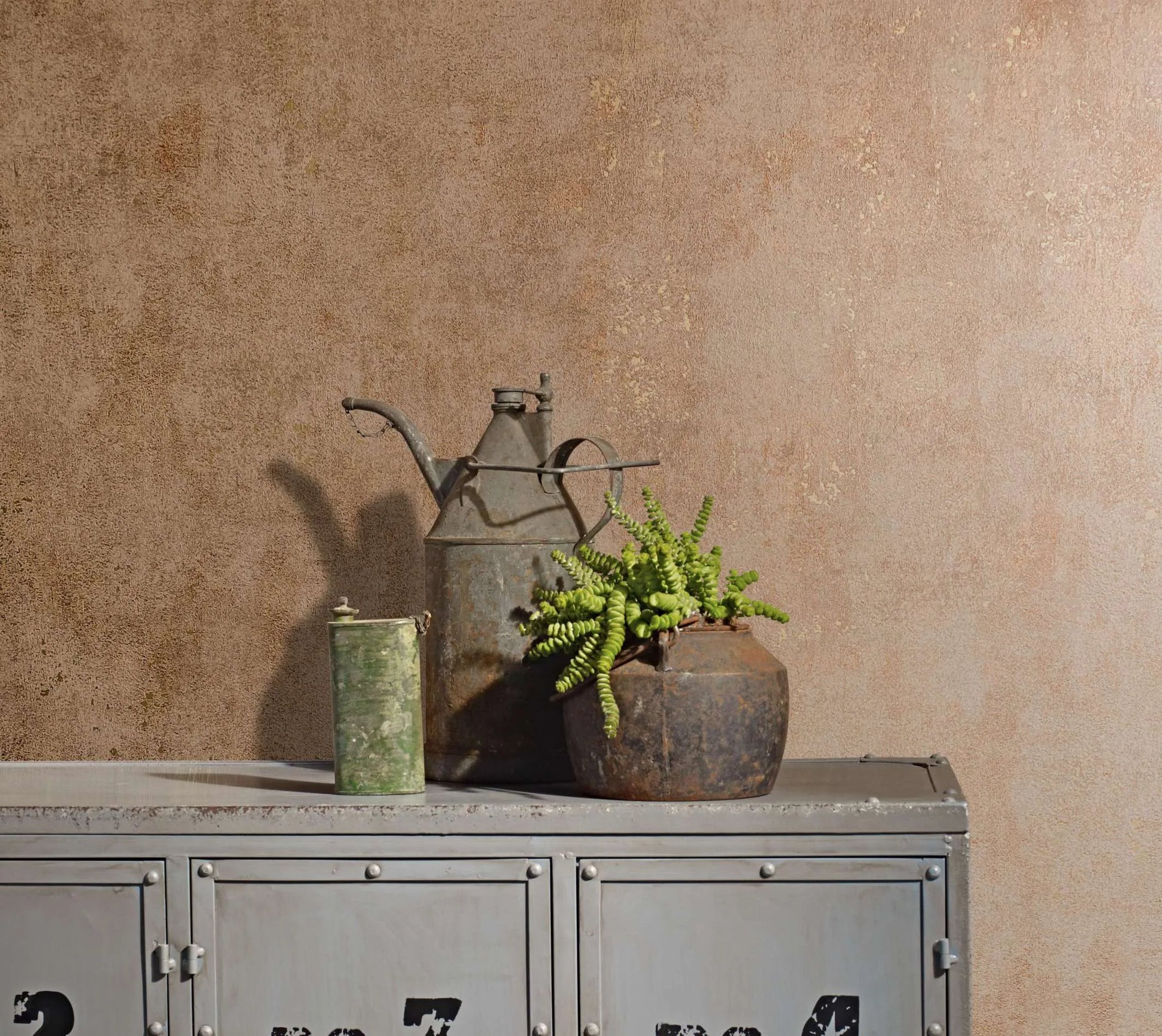 Marburg City Glow 34268 Tonal brown textured wallpaper behind a gray metal locker topped with a rusty watering can, a small green canister, and a potted plant.