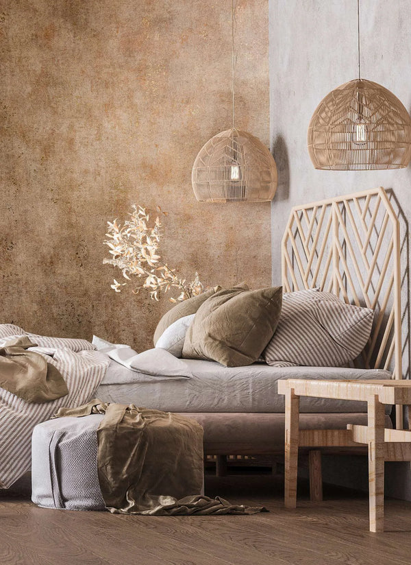 Marburg City Glow 34268 Textured mottled brown wallpaper on a bedroom accent wall, shown with a bed, geometric wood headboard, rattan pendant lights, a bench, and an ottoman.