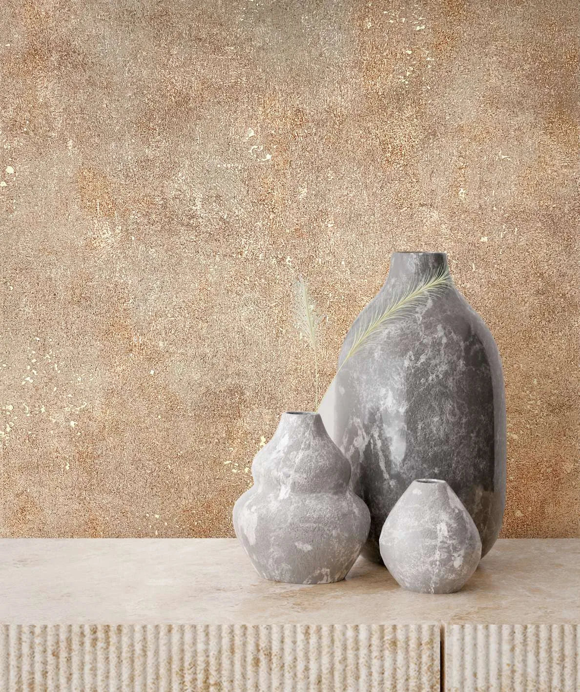 Marburg City Glow 34269 Textured beige and brown wallpaper with scattered gold flecks behind three gray stone vases on a ribbed stone console.