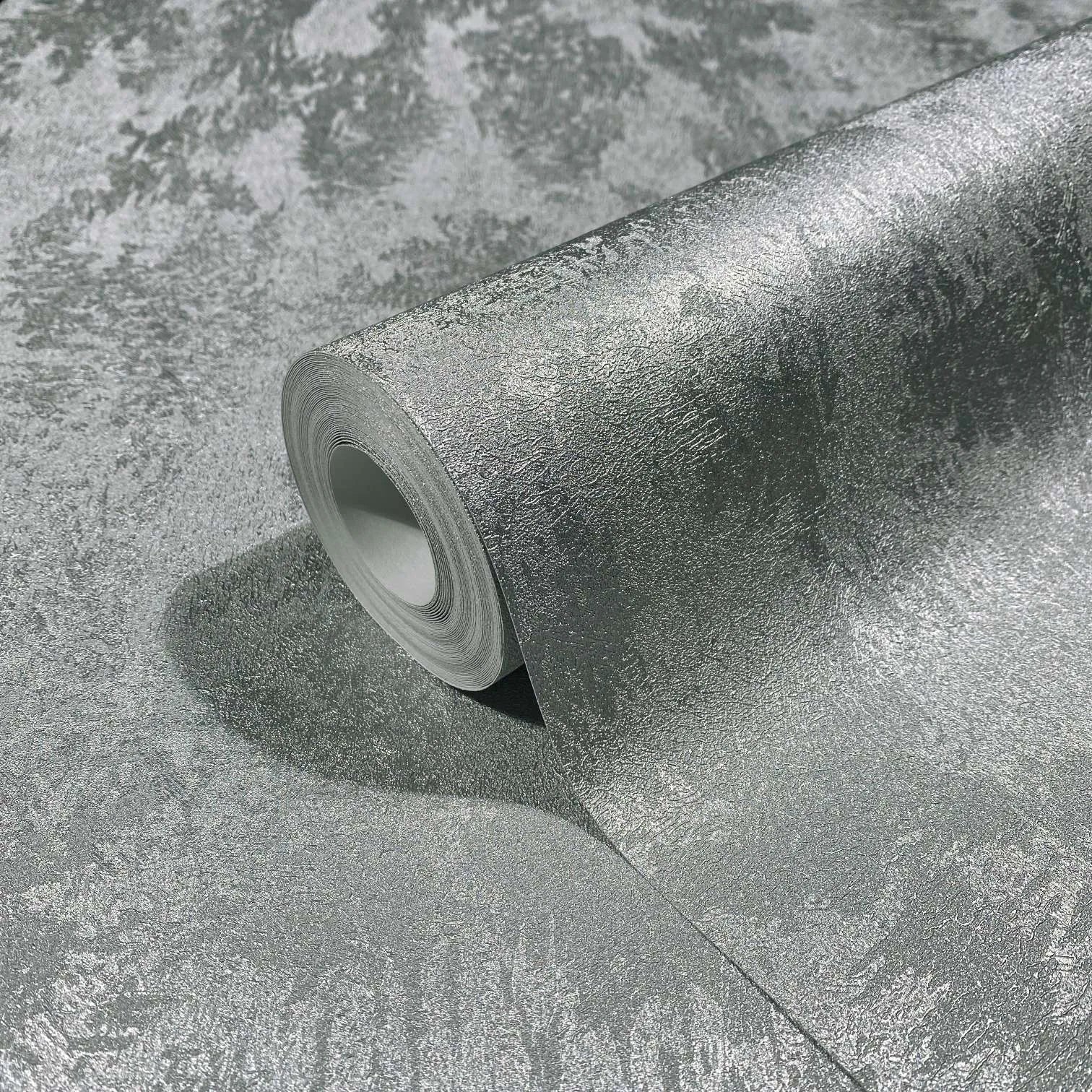 Marburg City Glow 34275 A metallic silver textured wallpaper roll partially unrolled on a matching surface, showing its irregular mottled pattern and sheen.