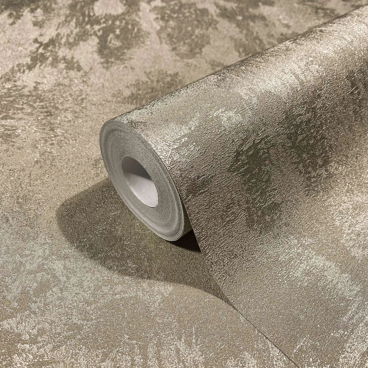 Marburg City Glow 34276 Close-up of a wallpaper roll resting on the same wallpaper, showing a mottled textured surface with a metallic sheen.