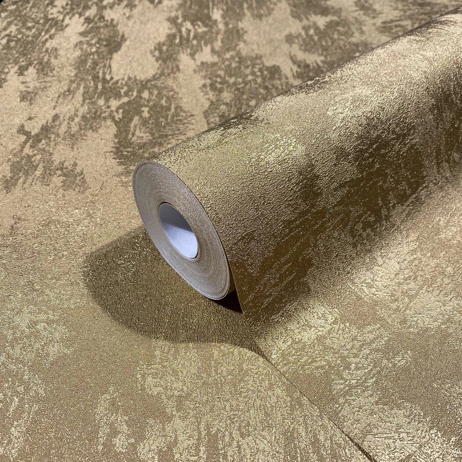 Marburg City Glow 34280 Close-up of a gold textured wallpaper roll resting on the same pattern, showing an irregular mottled finish with a soft sheen.