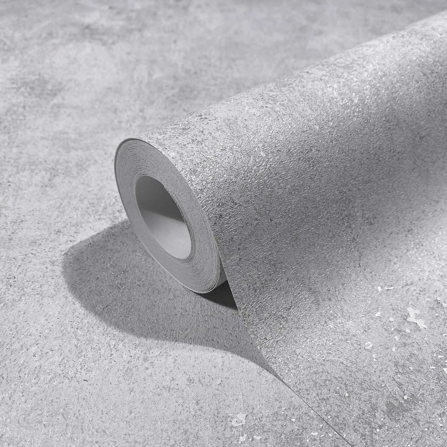 Marburg City Glow 34281 Close-up of a gray textured wallpaper roll partially unrolled on the same material, showing a concrete-like surface with fine speckling.