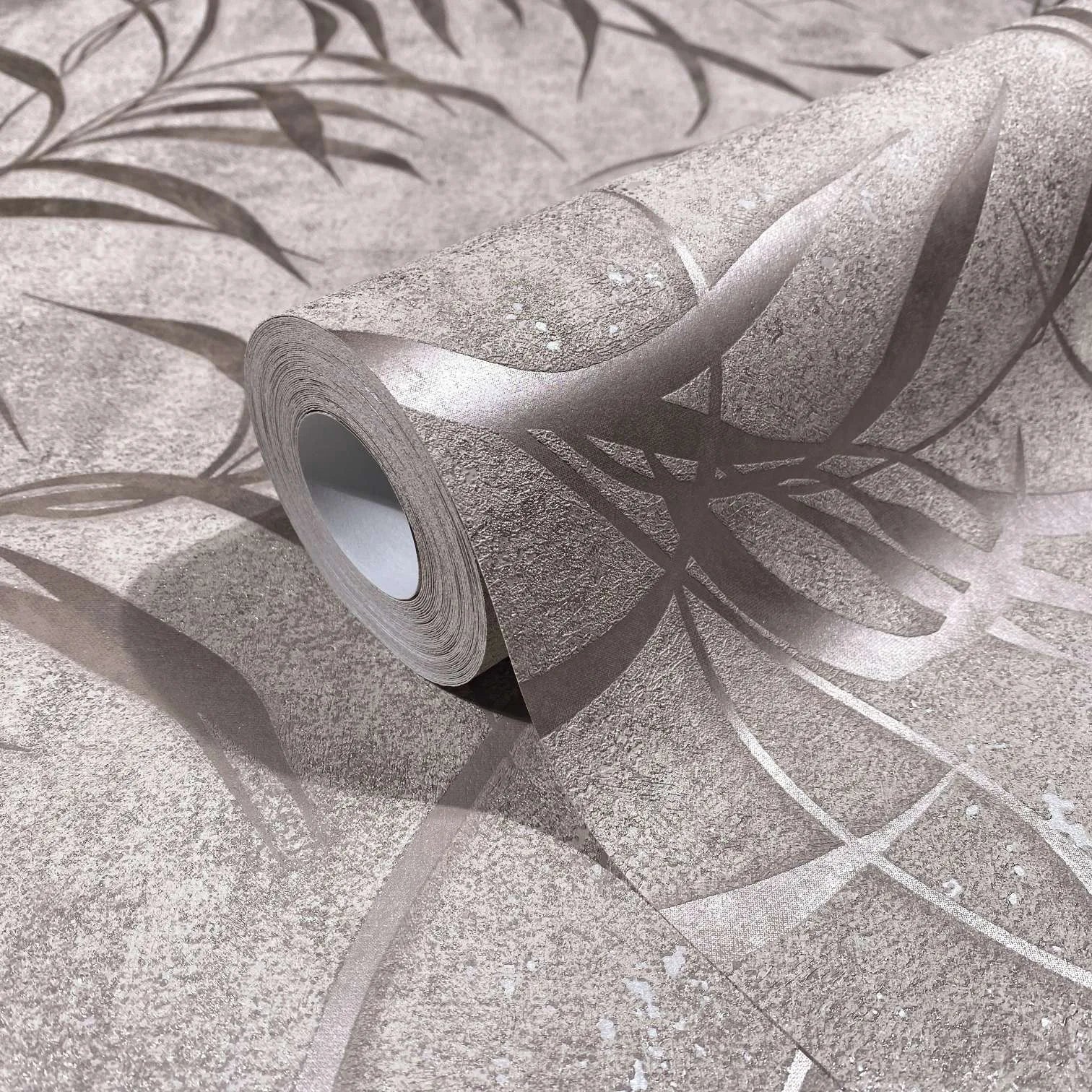 Marburg City Glow 34285 Close-up of a wallpaper roll resting on matching wallpaper, showing abstract curved metallic lines on a textured neutral background.
