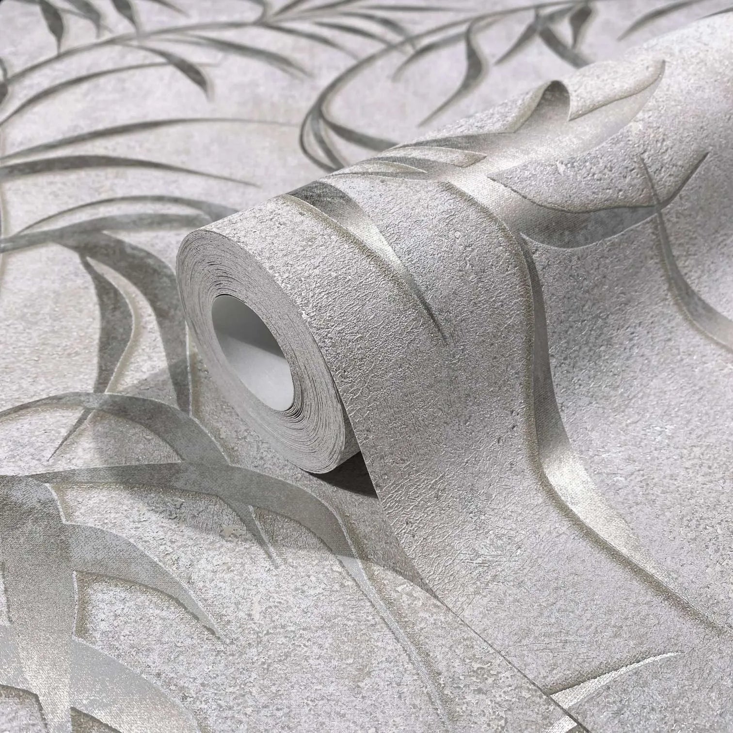 Marburg City Glow 34286 Close-up of a wallpaper roll with a light gray textured background and raised metallic silver curved lines, partially unrolled on a matching surface.