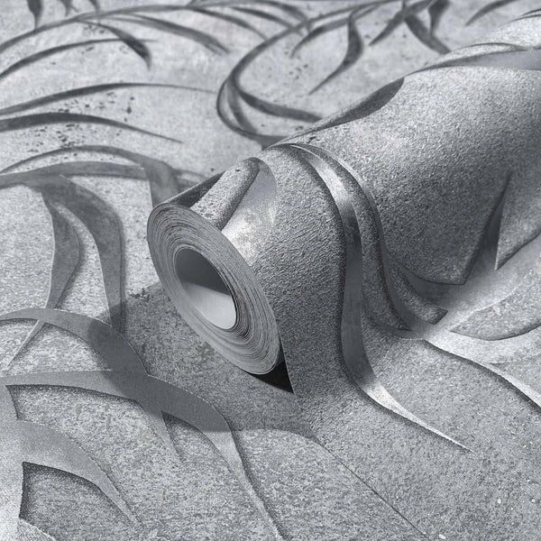 Marburg City Glow 34287 Close-up of a wallpaper roll resting on matching wallpaper, showing an abstract curved ribbon pattern with raised detailing in gray and silver tones.