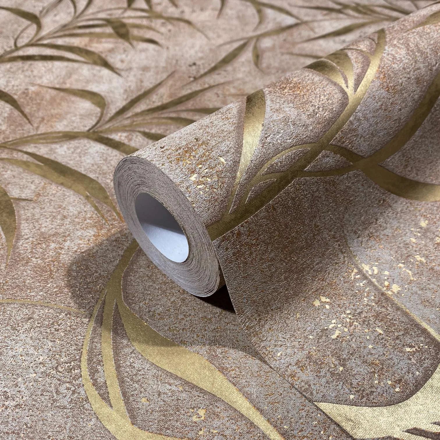 Marburg City Glow 34288 Close-up of a wallpaper roll resting on the same pattern, showing a mottled brown background with sweeping gold curves and leaf-like shapes.