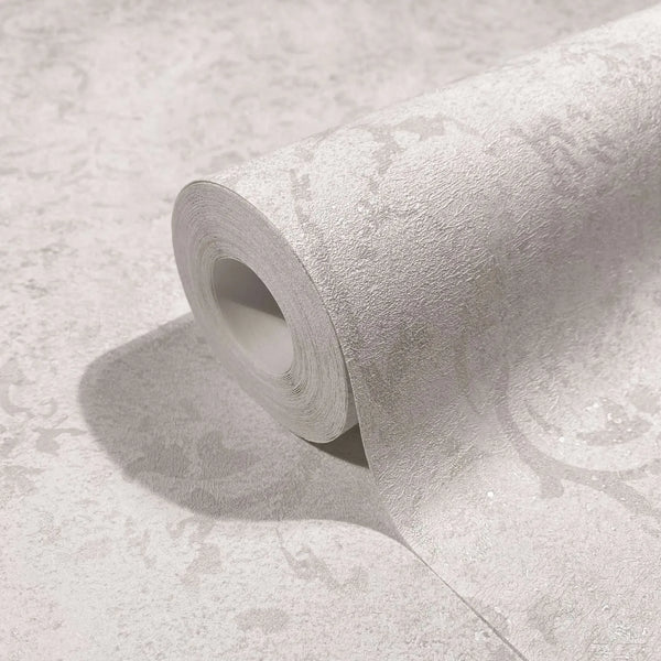 Marburg City Glow 34290 Close-up of a wallpaper roll resting on matching surface, showing light-toned textured wallpaper with a subtle tonal scroll pattern and soft sheen.