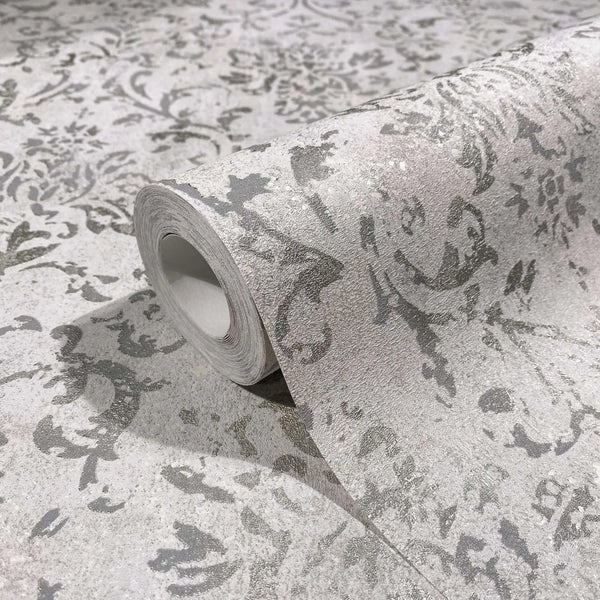 Marburg City Glow 34292 Close-up of a wallpaper roll showing a gray distressed damask pattern on a matching unrolled sheet.