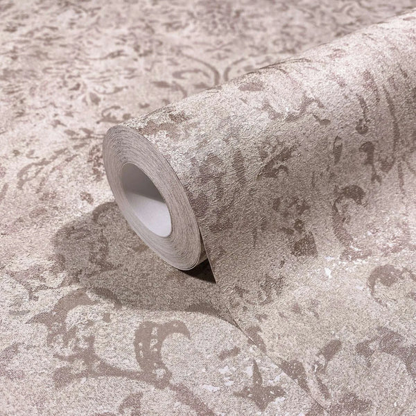 Marburg City Glow 34293 Close-up of a wallpaper roll resting on matching unrolled paper, showing a mottled textured scroll pattern in light brown tones.