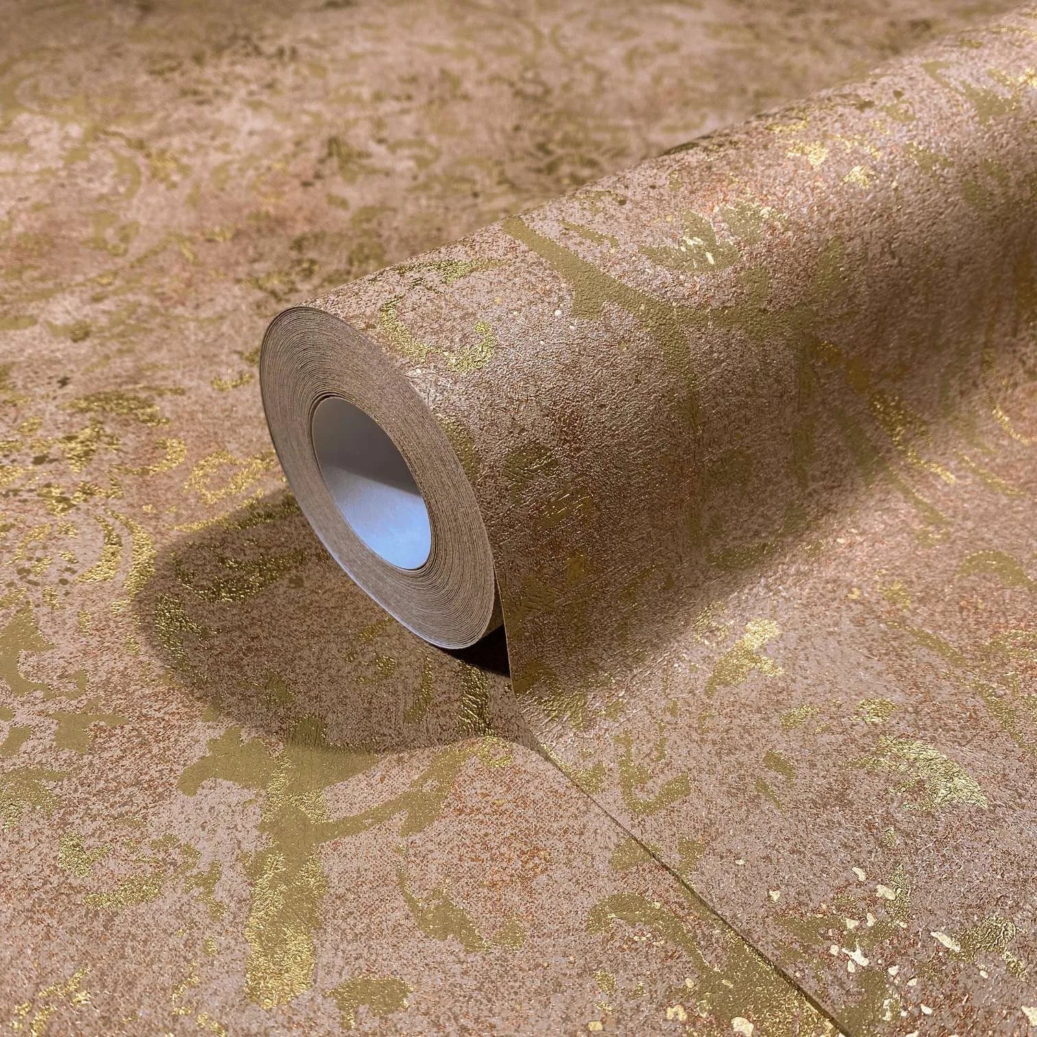 Marburg City Glow 34295 A brown wallpaper roll with metallic gold distressed scrolls, shown partially unrolled on a matching surface.