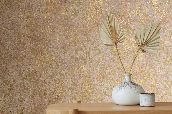 Marburg City Glow 34295 Close-up of brown wallpaper with a metallic gold damask pattern behind a white ceramic vase holding dried palm leaves on a wooden table with a small cup.
