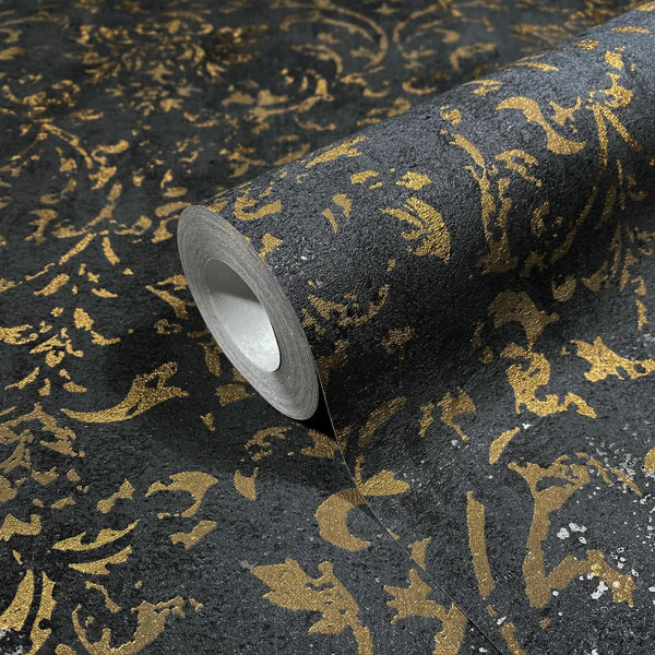 Marburg City Glow 34297 Close-up of a wallpaper roll with a metallic gold damask pattern on a dark textured background, shown partially unrolled.