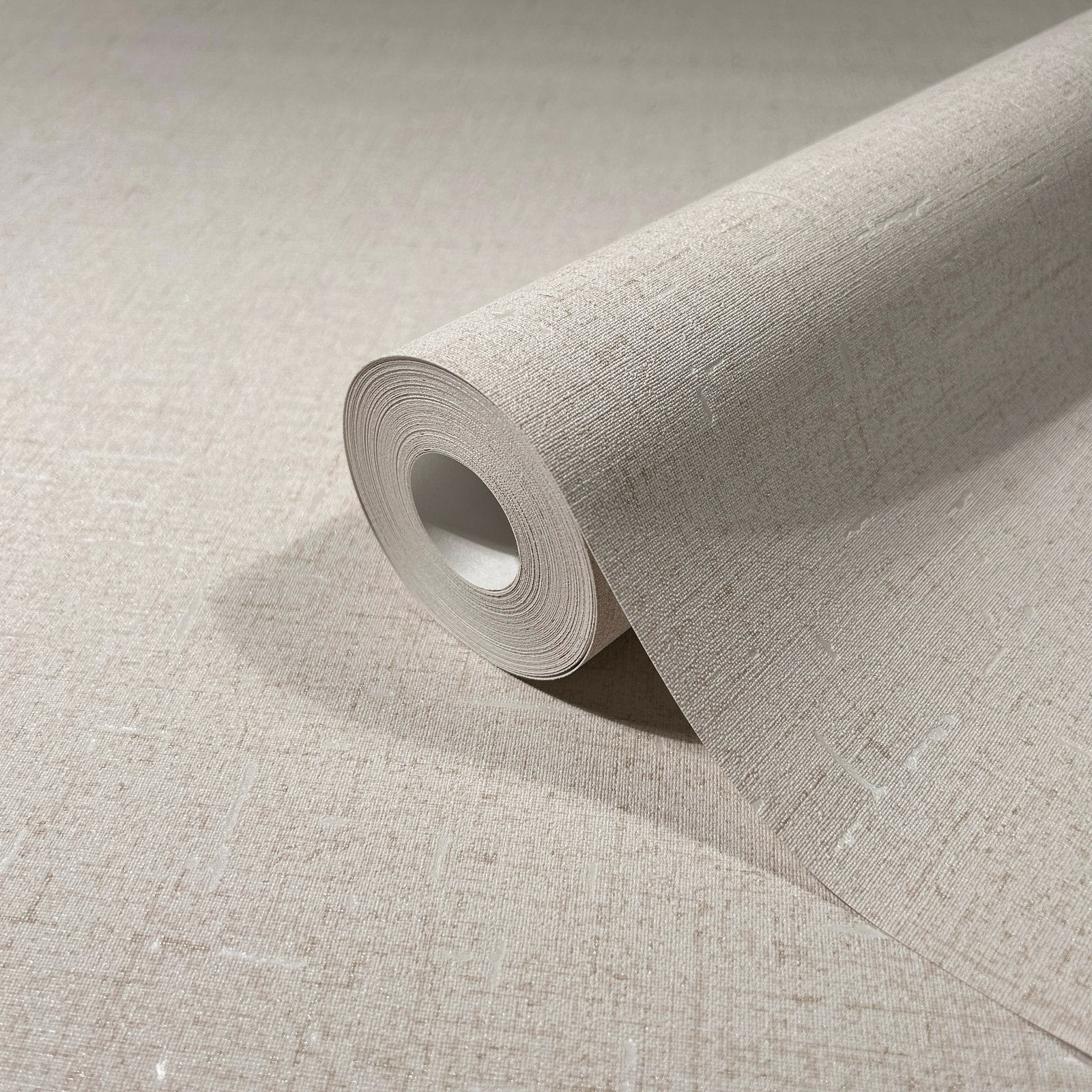 Marburg City Romance 35107 A beige textured wallpaper roll partially unrolled on a matching surface, showing a fine linen-like crosshatch pattern with small irregular slubs.
