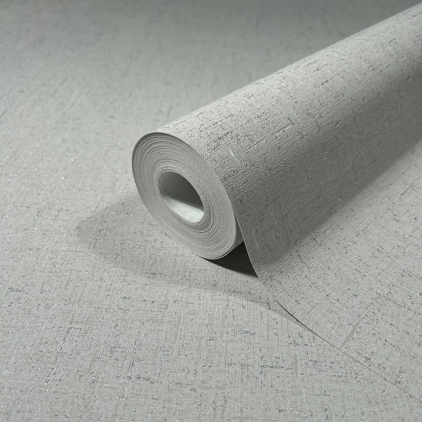 Marburg City Romance 35109 Close-up of a gray textured wallpaper roll with subtle metallic speckles, shown partly unrolled on the same pattern.