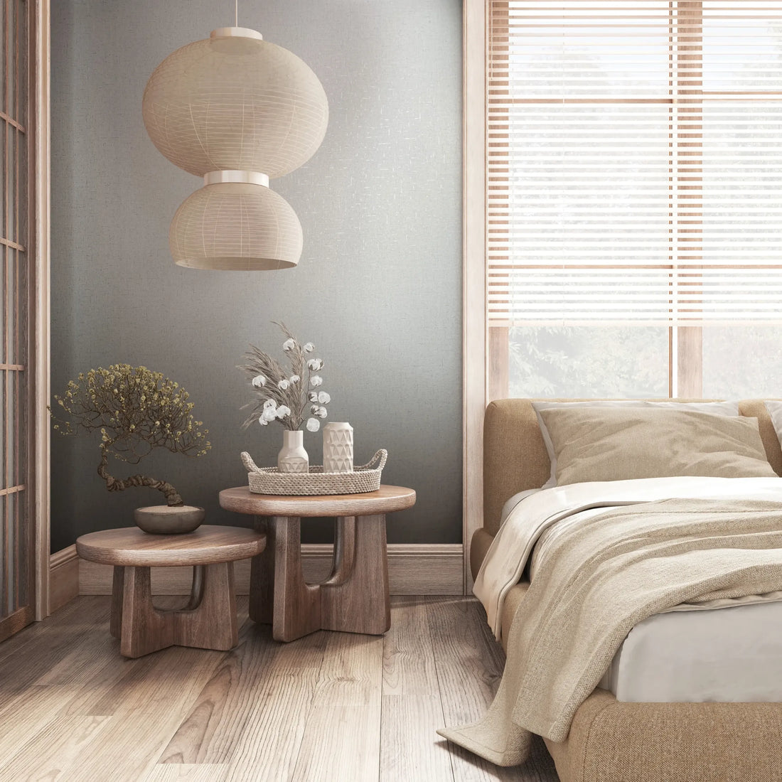 Marburg City Romance 35109 Gray textured wallpaper behind a cozy bedroom scene with a bed, two round wooden side tables holding a potted plant and vases on a woven tray, a pendant light, and a window with blinds.