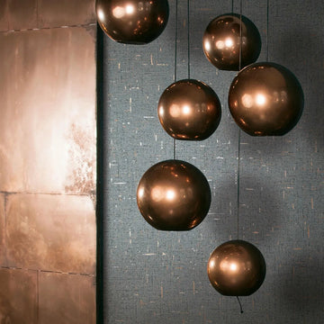 Marburg City Romance 35111 Textured dark grey wallpaper with small metallic flecks behind a cluster of bronze spherical pendant lights and a large metal wall panel.